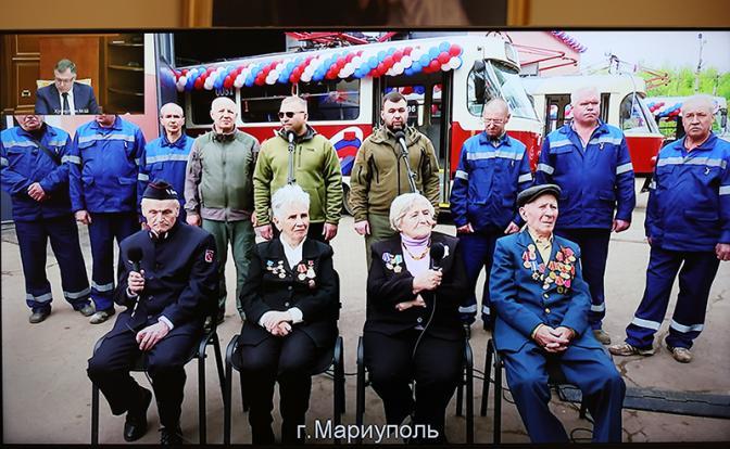 На фото: временно исполняющий обязанности главы ДНР Денис Пушилин (на экране в центре на втором плане) и другие участники церемонии запуска трамвайного движения в Мариуполе, в которой принял участие президент РФ Владимир Путин.
