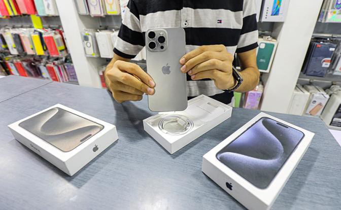 На фото: продавец смартфонов демонстрирует iPhone 15 Pro Max и iPhone 15 Pro в своем магазине