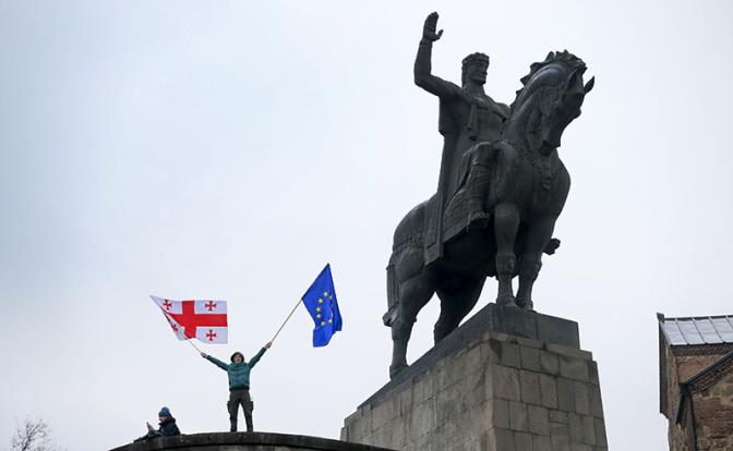 На фото: демонстрант размахивает флагами Грузии и ЕС у памятника царю Вахтангу Горгасали в центре Тбилиси, Грузия.