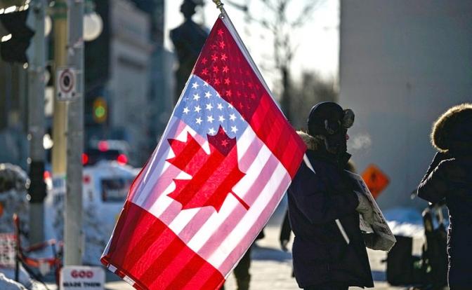 На фото: протестующий держит флаги Канады и США на Парламентском холме в Оттаве.