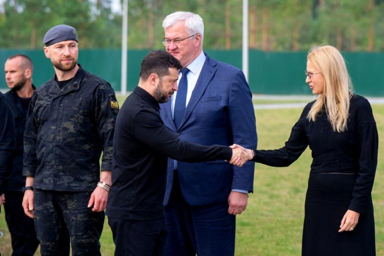 На фото: президент Украины Владимир Зеленский (слева) пожимает руку заместителю председателя парламента Украины Елене Кондратюк в присутствии исполняющего обязанности министра обороны Украины Евгения Хмары и исполняющего обязанности министра иностранных дел Украины Андрея Сыбиги (слева направо, сзади), август 2026 года.